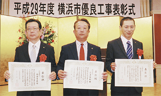表彰状を手にする倉澤俊郎社長（中央）と秀俊専務（左）、石井邦輝さん