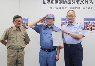 敬礼する枝太郎さん（中央）。左は有賀団長、右は小出健消防署長