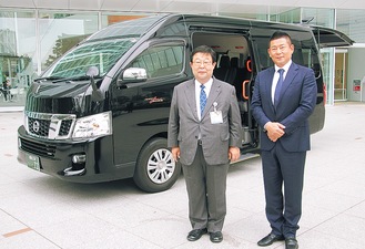 貸与する車両の前に立つ桑原社長（右）と田中局長