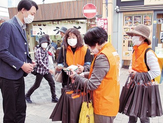 弘明寺商店街でオレンジ色のベストやリボンを配る区職員ら