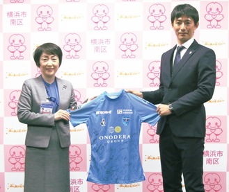 松山区長（左）に全選手のサイン入りユニフォームを渡す高橋選手