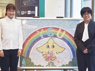 市大センター病院の本館入口に飾られている折り紙で作った市大のキャラクター「ヨッチー」などのモザイクアートの前で笑顔を見せる山中さん（左）と淺香さん