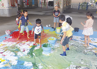３・６ｍ×５・４ｍの樹脂製のキャンバスに手や足を使い水性ペンキで多彩な色を塗る子どもたち