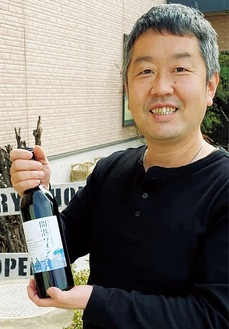自身が丹精込めて栽培したぶどうを原料に醸造された地場ワイン「開港ワイン」を手にする三村さん
