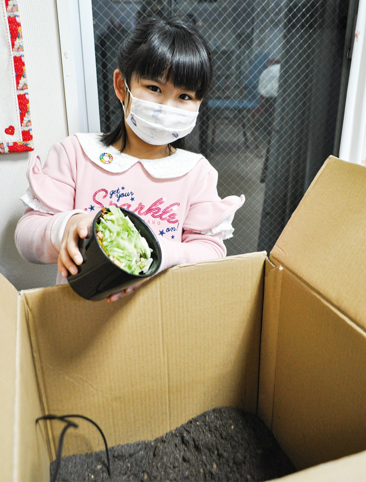 段ボールコンポストに野菜くずを投入する永井さん