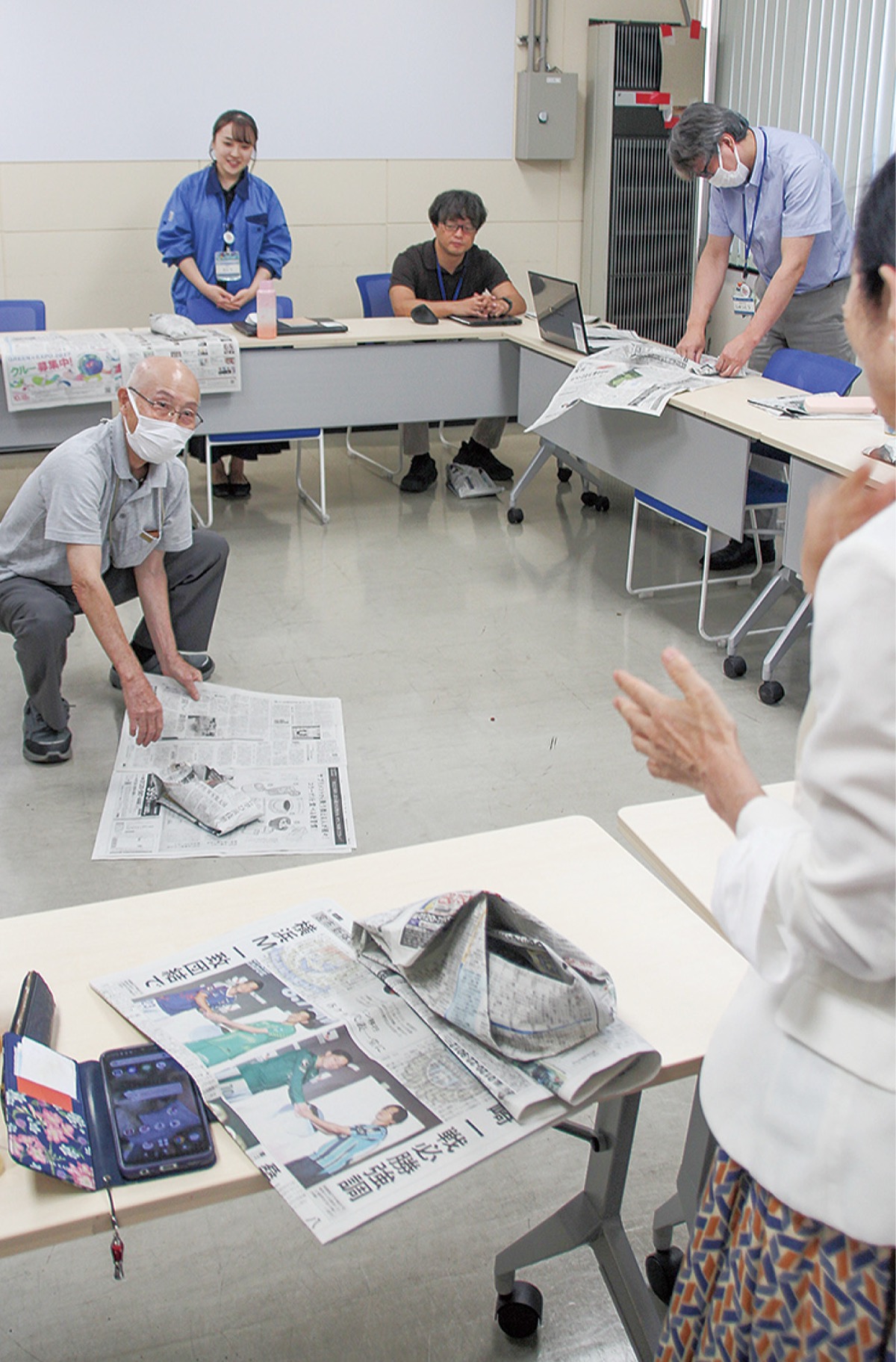 新聞紙でスリッパを作る運営委員ら