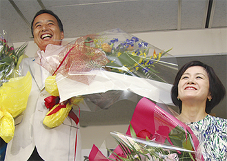 島村氏（左）は支持者から花束を受け取り笑顔（右は妻の奈津子さん）