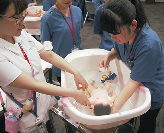 看護師の指導のもと、人形を使って沐浴の流れを体験する参加者＝同院提供