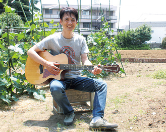 自身の畑でギターを弾く影山さん