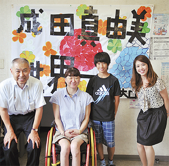 応援旗を前に成田さん（左から2番目）を囲む学校関係者