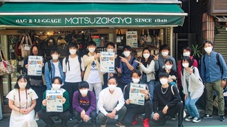 六角橋商店街の店舗にチラシの掲示を行う同フォーラムの学生と野村代表理事（前列中央）