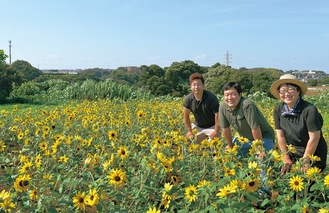 ひまわり畑を紹介する３人。右から石川綾乃さん、穣さん、土志田さん＝７月22日撮影