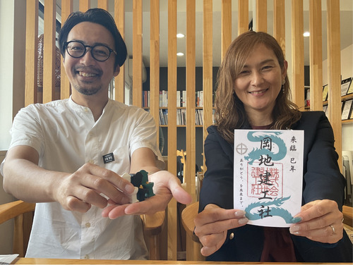 ガチャガチャを持つ岡地代表と御朱印を持つ社員の細川さん