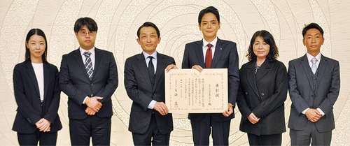 表彰状を手にする長谷川代表取締役（左から３人目）と山中市長（右から３人目）