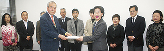メンバーの前で宮崎委員長（中央左）が野本区長（同右）に提案書を手渡した