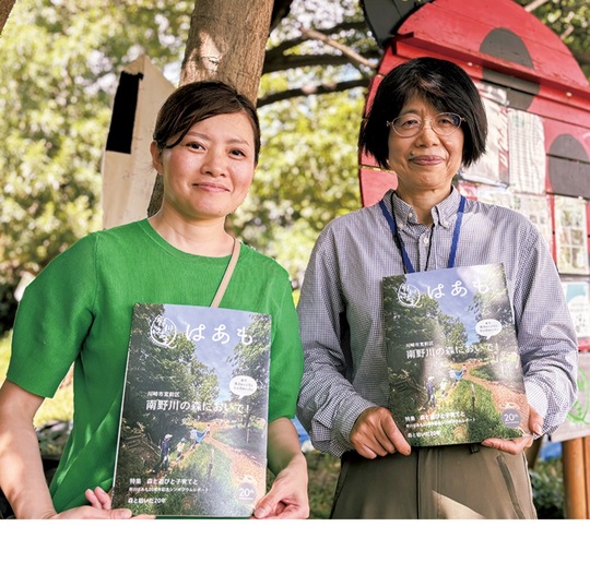 森の中で冊子を手にする奥さん（左）と伊藤会長