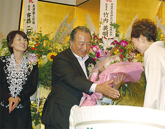 花束を受け取る大島明氏（中央）、左はまみ子夫人
