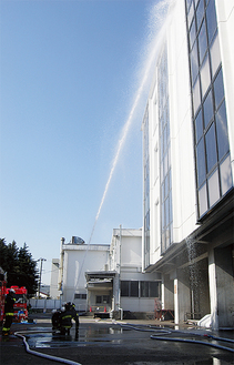 消防隊員たちが工場に向けて放水。ホースをつなぎ、高さ約15メートルまで水を噴き上げた