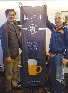 参加店の目印となる幟を持つ阿部さん（右）と街おこし協力隊の浅井さん