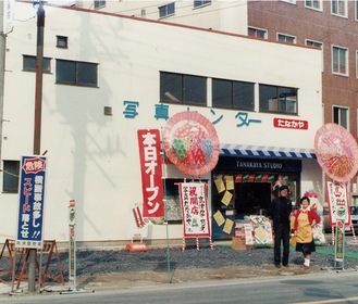 開店当時、店先に並ぶ鈴木克明代表と寄里枝さん