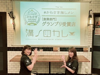 グランプリ受賞店の証となるデザインを前に笑顔をみせる平澤舞子店長（左）と平野阿也副店長（右）
