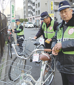 自転車や二輪車に犯罪抑止を促す荷札を取り付ける防犯指導員たち（先月30日、登戸駅周辺で）