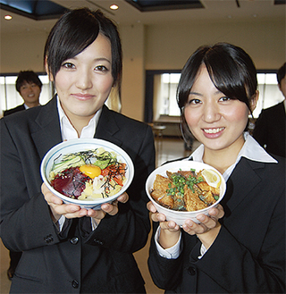 半年以上かけて開発したフィッシュ丼（右）とユッケ丼（左）を手にする学生