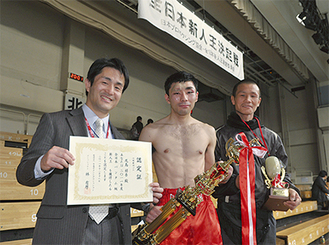 試合後トロフィーを手にする尾島選手（中央）と新田会長（左）、孫トレーナー（右）　写真は山口裕朗さん提供