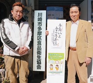 看板を手にする小出会長(右)、指導部長の鈴木大輔さん＝16日