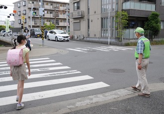 踏切付近の横断歩道で、通行人の安全を見守る登戸多摩川町会の役員＝きのう28日