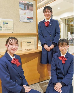 自作の啓発ポスターとクライメートクロックを囲む、(左から)級友の須崎さん、村松さん、島田さん