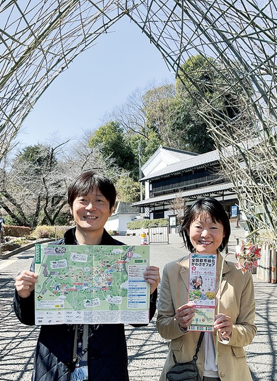 生田緑地会場入口に設けられた竹のゲートの下で、公式マップと竹材のかざぐるまを紹介する市の担当者