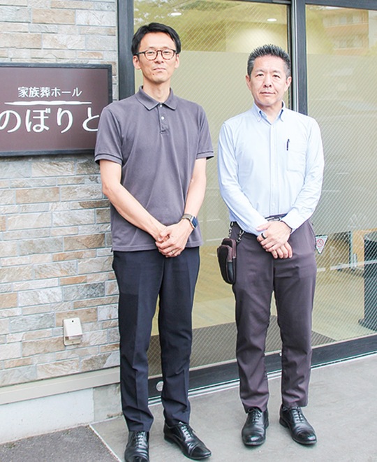 会場となっている葬儀式場の入口に立つ吉澤さん（右）と吉澤企画社員の多田総太郎さん