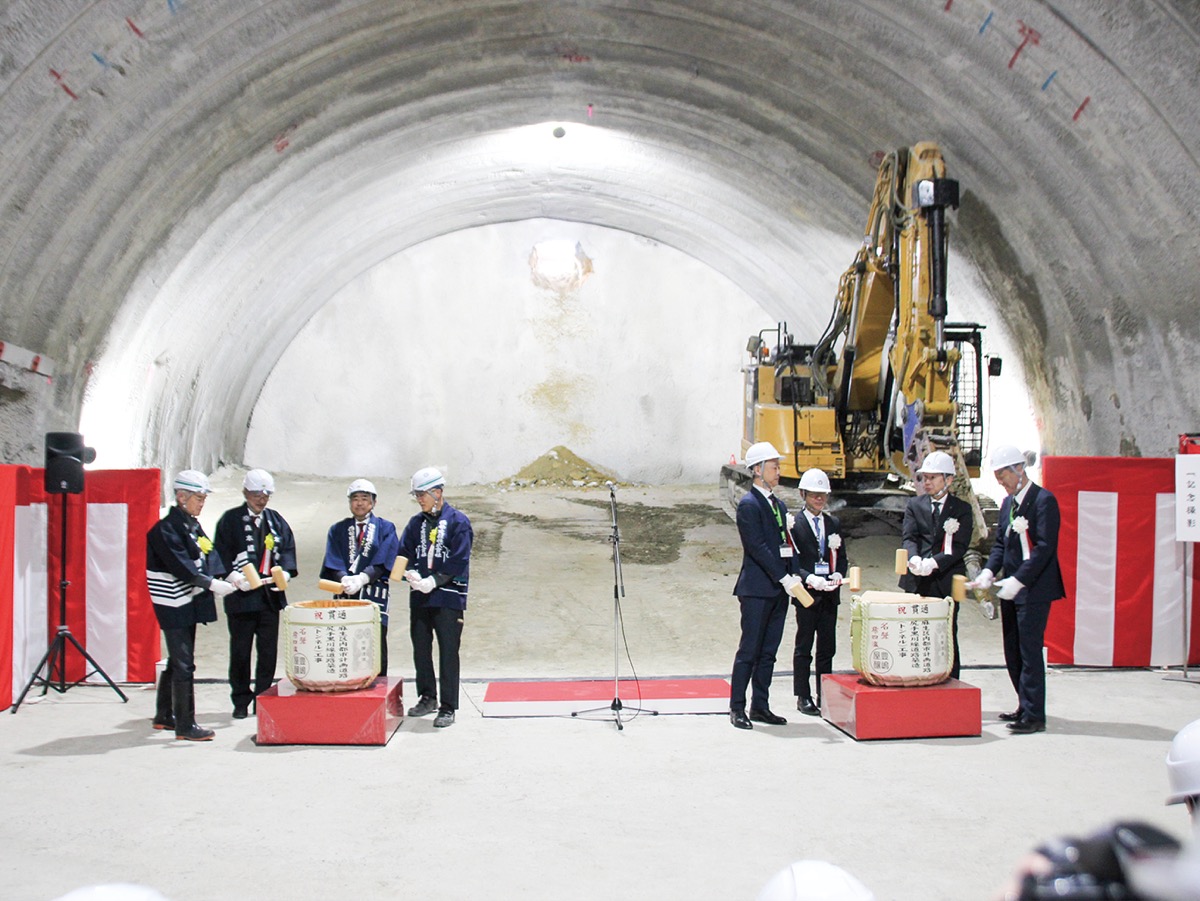 貫通したトンネル壁の前で鏡開きを行う工事関係者ら