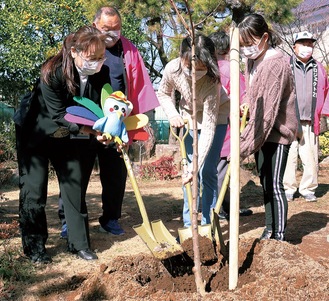 桃の木を植樹する児童と八幡校長（左）