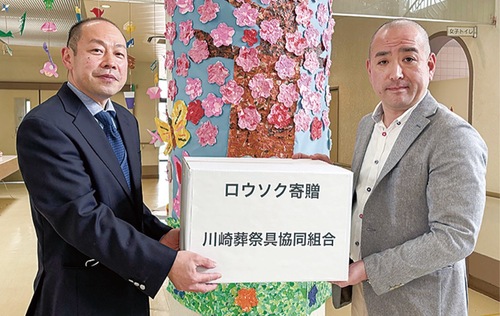 取手市立障害者福祉センターふじしろの小林一郎施設長にロウソクを手渡す齋藤理事長(右)