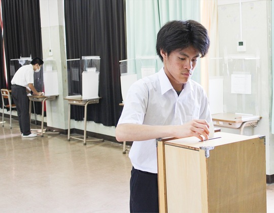 木製の投票箱に１票を投じる生徒