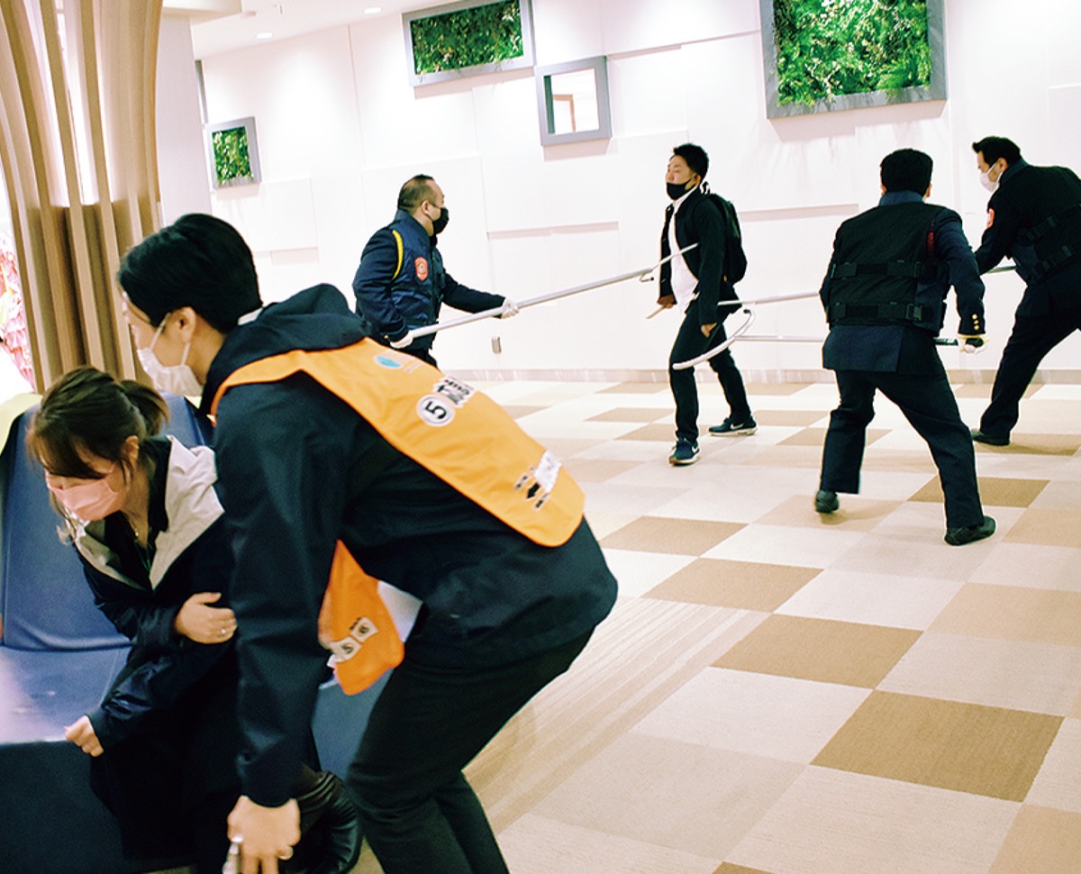 ケガ人役を救護するスタッフ（手前）と犯人役を取り押さえる警備員（奥）