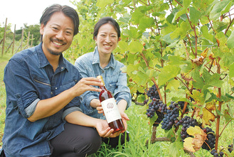 収穫前のブドウ畑で出来たばかりのワインを手にする山田さん（左）と妻のみずほさん