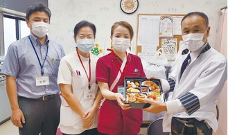 弁当を手渡す宮川さん（右）と病院スタッフ