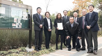 掲示板の前で福田所長（左から２番目）を囲む会員