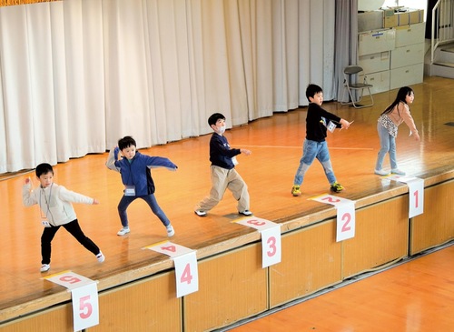 ステージの上から紙飛行機を飛ばす児童ら
