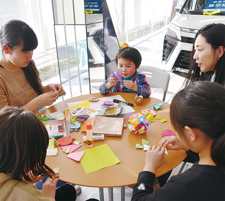 来店した親子連れに折り紙を教える和泉短大の学生（左）＝９日、ウエインズ上鶴間店