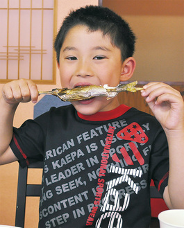 自分で串焼きにした鮎を頬張る子ども＝６月22日、割烹旅館旭屋