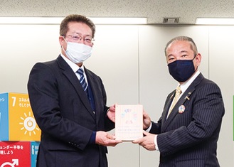 昨年12月に行われた交付式で本村賢太郎市長（右）から登録証盾を受け取る原理事長