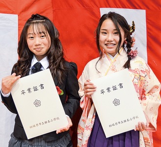 バナナペーパーの証書ホルダーを手に笑顔の卒業生＝３月23日、田名小学校