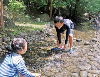 同公園内を流れる小川で水をかけあう子どもたち＝24日