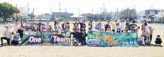 完成した横断幕を広げ笑顔の児童たち。「One Team」と書かれたのは１組が、「みんなの応援が勝利につながる」と書かれたのは２組が製作＝24日、田名北小学校
