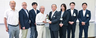 日本酒を本村市長に手渡す石井会長（左から4人目）