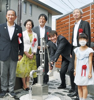 井戸水をくむ柴田社長（右から３人目）。左端が本村市長。右端はグループ会社社員の家族で１号機設置の際も「モデル」となった植木紬さん